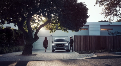 Vue d'un Volvo XC60 hybride rechargeable en charge devant un garage de copropriété avec une femme et un homme de qui vont monter à bord
