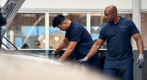 Deux mécaniciens Volvo en intervention sur le capot avant ouvert d'un véhicule en atelier