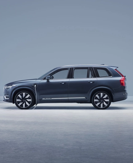 XC90 Hybride rechargeable à transmission intégrale Bleu Denim avec roues 21" en vue latérale à l'intérieur d'un studio et connecté à une borne de recharge.