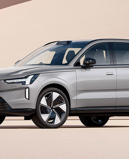 Volvo EX90 argenté garé devant un mur beige avec une ombre projetée