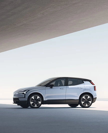 Vue latérale d’une Volvo EX30 blanche moderne avec toit noir et grandes roues, dans un décor minimaliste