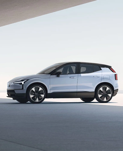 Vue latérale d’un Volvo EX30 blanc moderne avec toit noir et grandes roues, dans un décor minimaliste