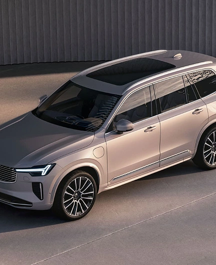 Volvo XC90 beige stationné sur une surface en béton, vu en plongée, avec design moderne et mur incurvé en arrière-plan