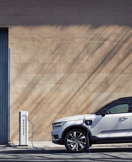 XC40 branchée à une borne de recharge avec câble bleu, stationnée devant un mur beige et une porte bleue