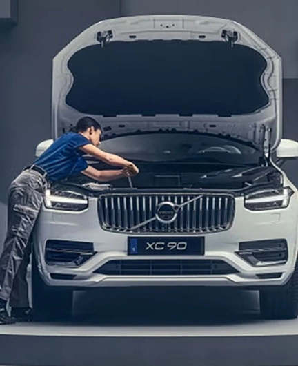 Personne inspectant le moteur d’un Volvo XC90 blanc sur une plateforme circulaire dans un décor minimaliste