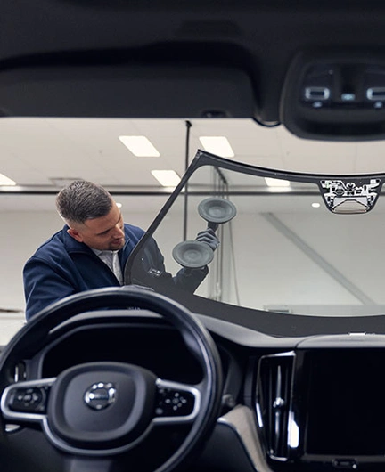 Deux techniciens installent un pare-brise sur une voiture, vu de l’intérieur du véhicule.