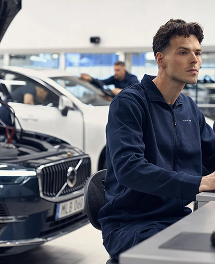 Un technicien devant son ordinateur inspecte le boitier informatique du Volvo XC60 placé derrière lui avec le capot ouvert