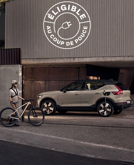 Femme avec vélo devant une Volvo EX40 électrique en charge dans une allée.
