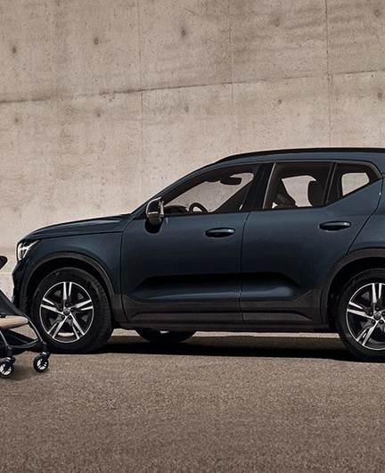 Une femme en imperméable tenant une poussette se tient debout devant un XC40 Volvo bleu