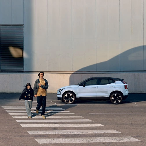Deux personnes traversent un passage piéton, Volvo EX30 blanche en arrière-plan projetant une ombre sur le mur