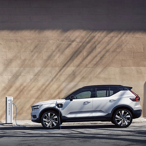 XC40 branchée à une borne de recharge avec câble bleu, stationnée devant un mur beige et une porte bleue