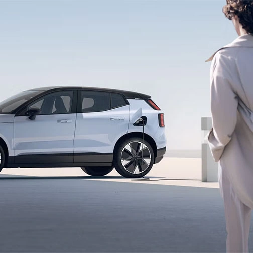 Volvo EX30 en charge, observé par une personne en manteau beige.