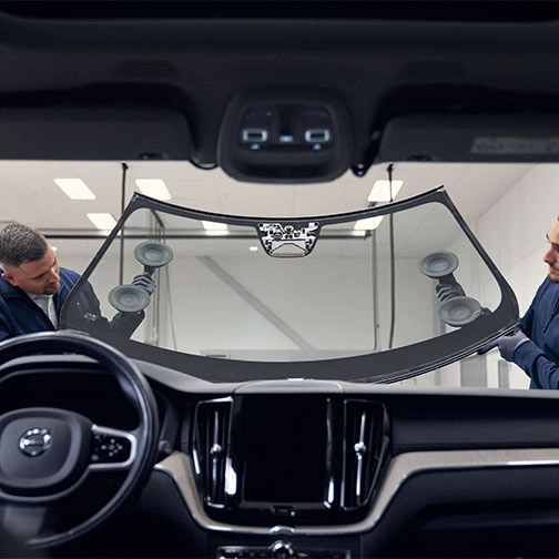 Deux techniciens installent un pare-brise sur une voiture, vu de l’intérieur du véhicule.