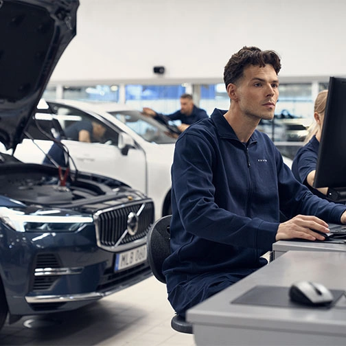 Un technicien devant son ordinateur inspecte le boitier informatique du Volvo XC60 placé derrière lui avec le capot ouvert