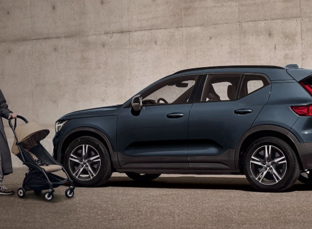 Personne avec une poussette près d’un SUV Volvo XC40 Denim garé devant un mur en béton.