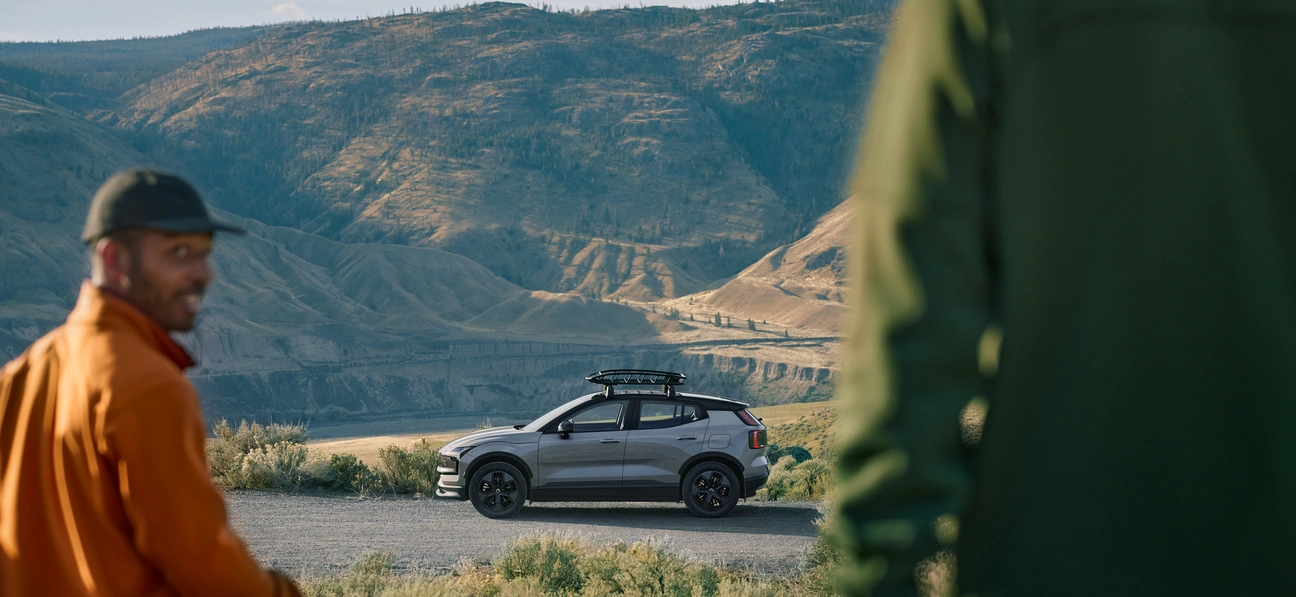 Voiture EX30 Cross Country dans la nature avec deux personnes qui se dirigent vers ce petit SUV 100% électrique
