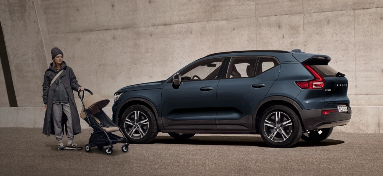 Personne avec une poussette près d’un SUV Volvo XC40 Denim garé devant un mur en béton.