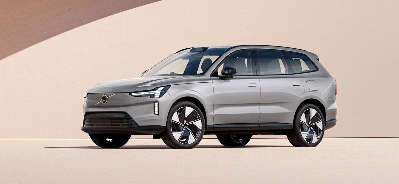 Volvo EX90 argenté garé devant un mur beige avec une ombre projetée