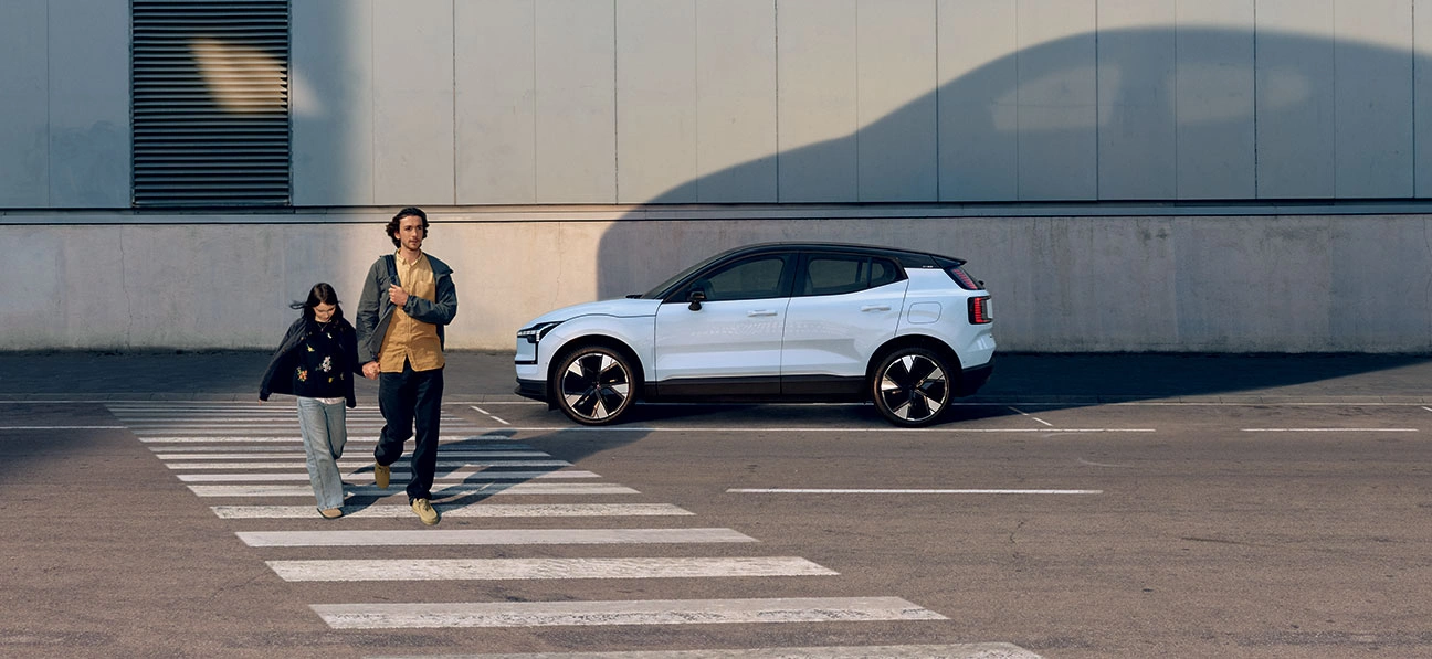 Deux personnes traversent un passage piéton, Volvo EX30 blanche en arrière-plan projetant une ombre sur le mur