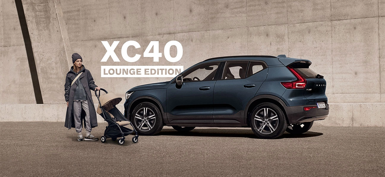 Volvo XC40 Lounge Edition garé près d’une personne avec une poussette devant un mur en béton