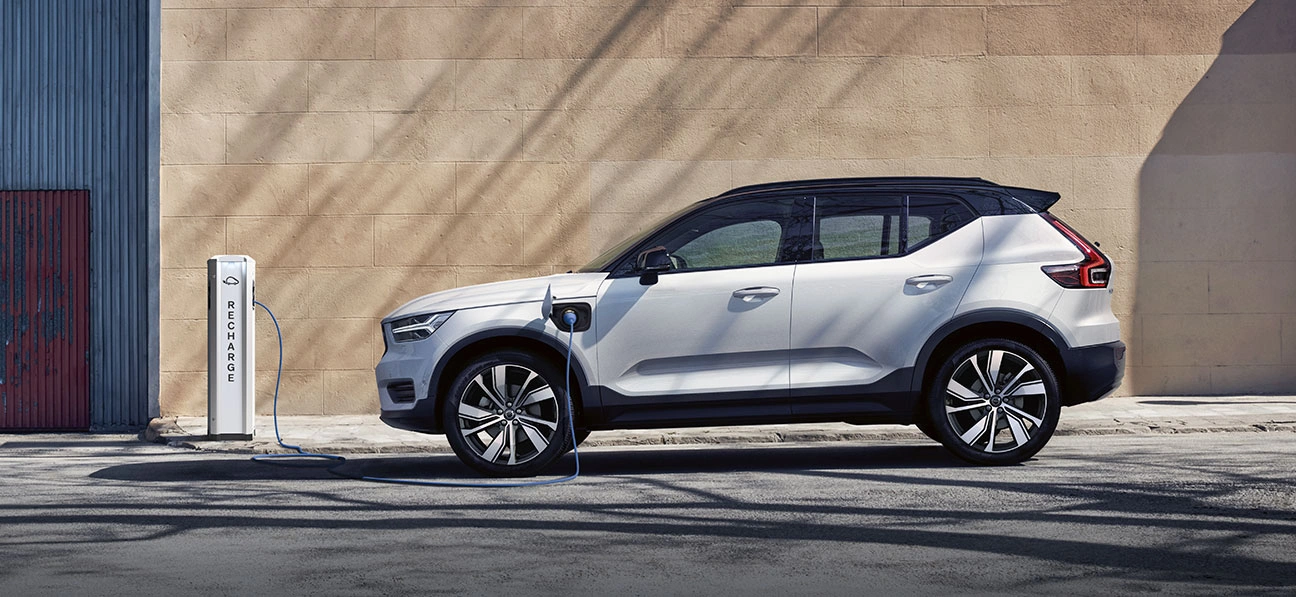 XC40 branchée à une borne de recharge avec câble bleu, stationnée devant un mur beige et une porte bleue