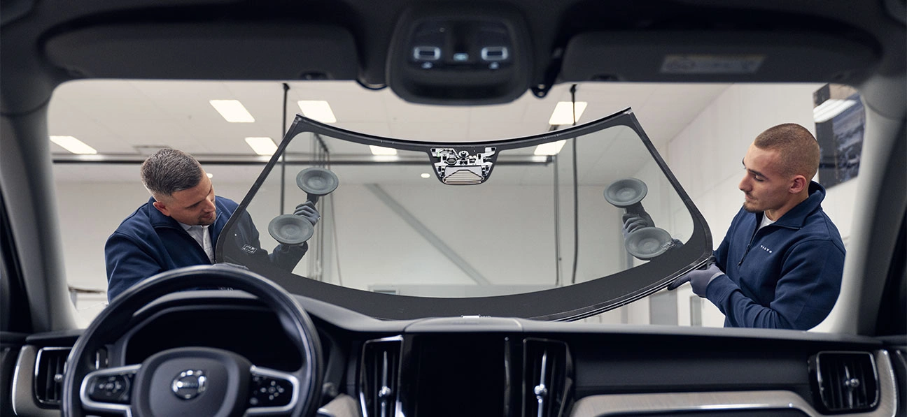 Deux techniciens installent un pare-brise sur une voiture, vu de l’intérieur du véhicule.
