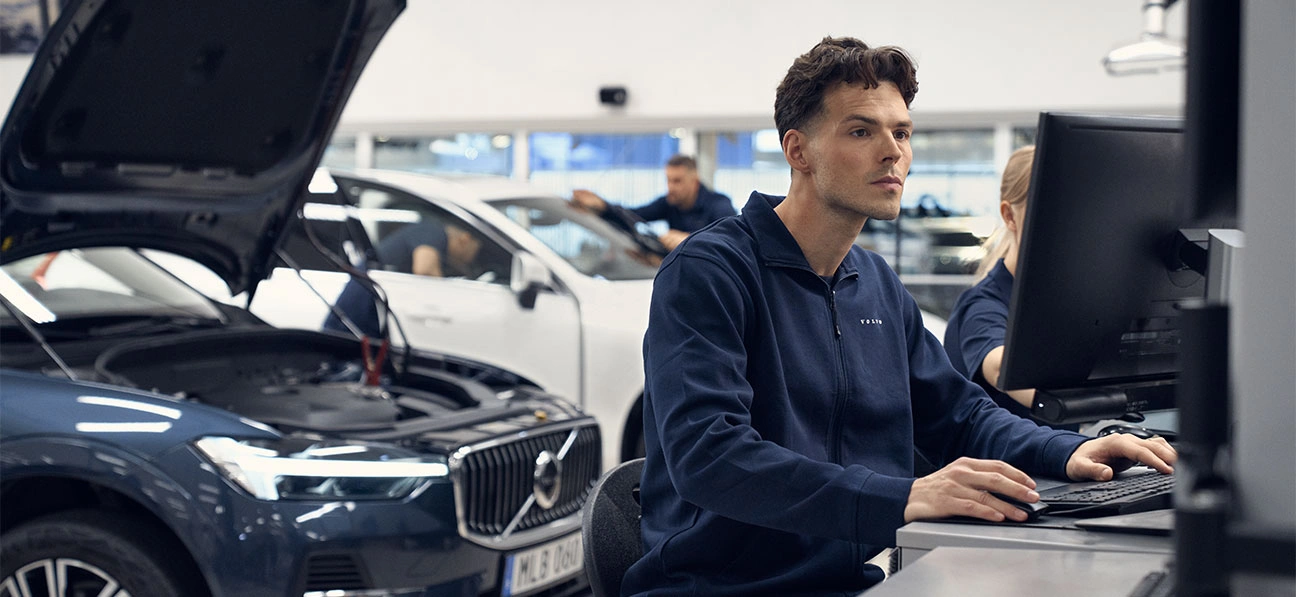 Un technicien devant son ordinateur inspecte le boitier informatique du Volvo XC60 placé derrière lui avec le capot ouvert