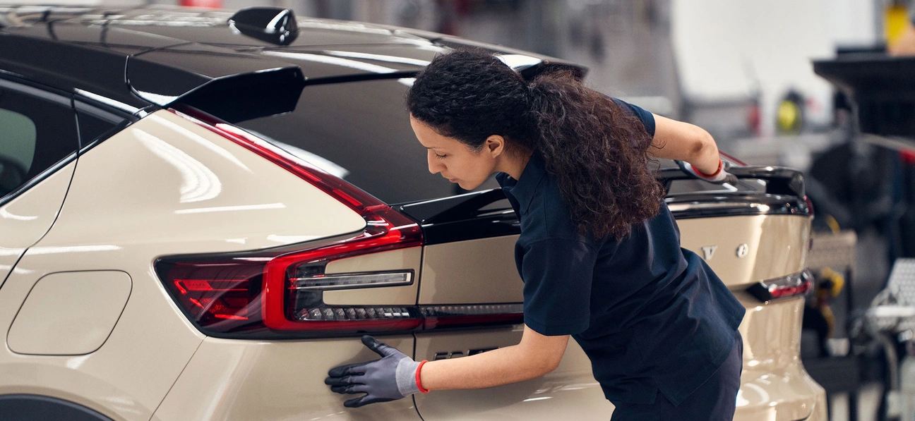Personne inspectant l’arrière d’un SUV Volvo beige et noir dans un atelier de réparation automobile.