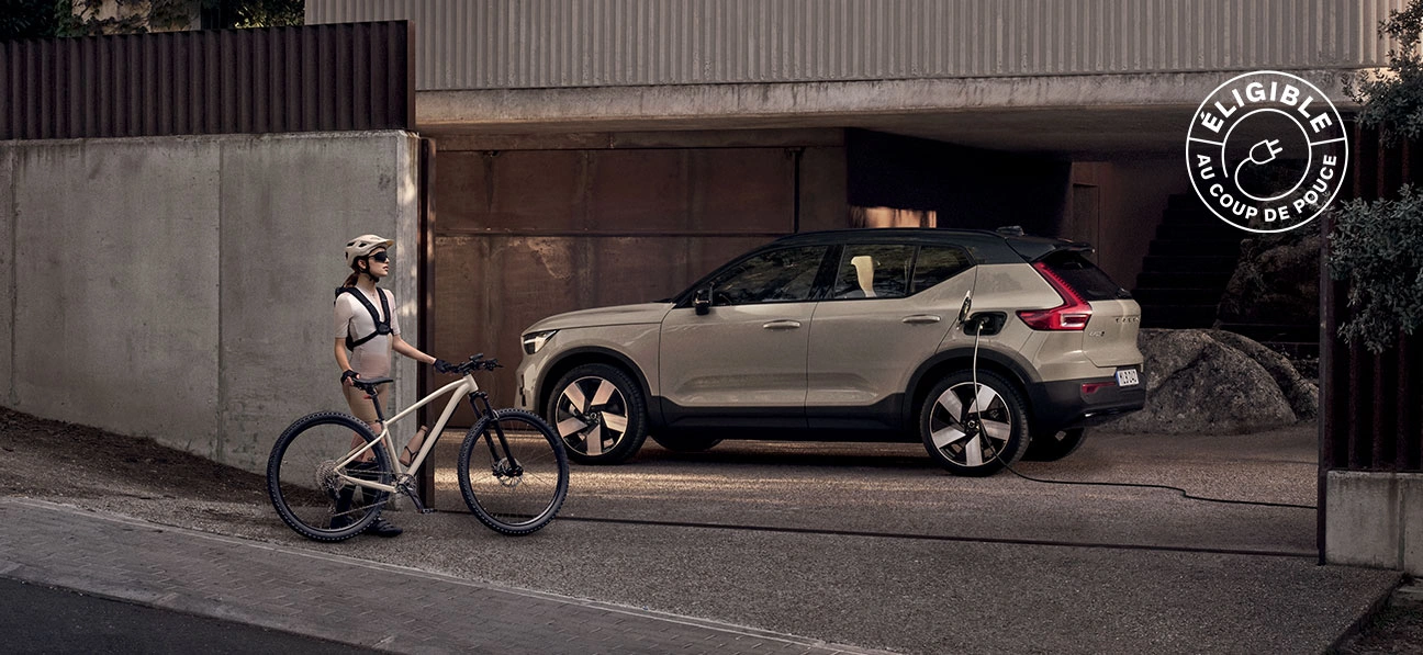 Femme avec vélo devant une Volvo EX40 électrique en charge dans une allée.