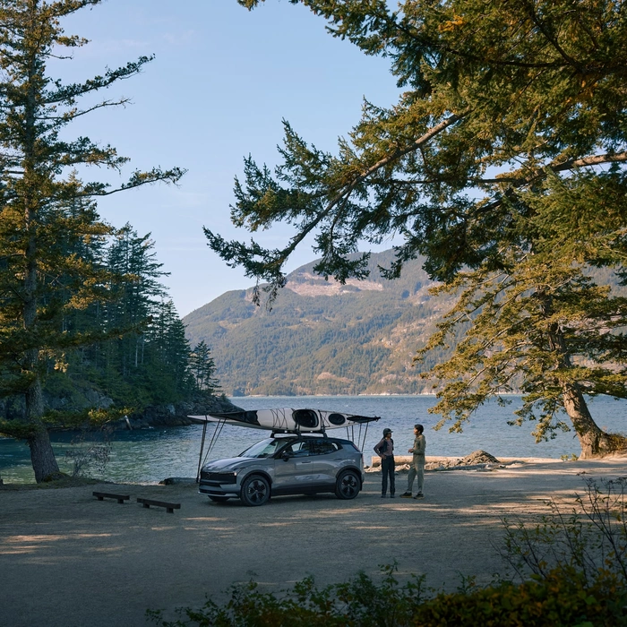 SUV EX30 Cross Country garé devant un lac avec unkayak sur le toit et deux personnes à côté qui discutent 