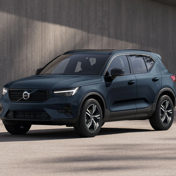 SUV compact Volvo XC40 bleu denim, garé sur fond béton, vue trois quart avant gauche