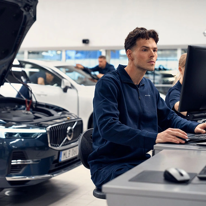 Un technicien devant son ordinateur inspecte le boitier informatique du Volvo XC60 placé derrière lui avec le capot ouvert