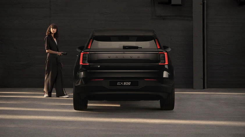 Volvo EX30 Black Edition vu de l’arrière, garé devant un mur sombre avec une personne à côté