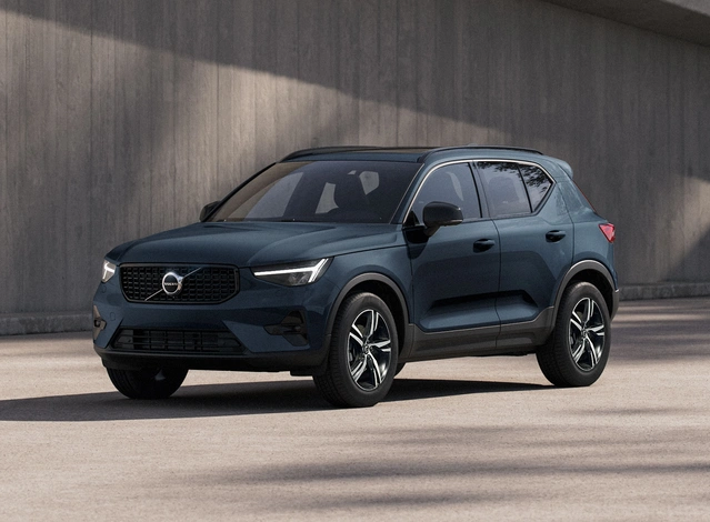 SUV compact Volvo XC40 bleu denim, garé sur fond béton, vue trois quart avant gauche
