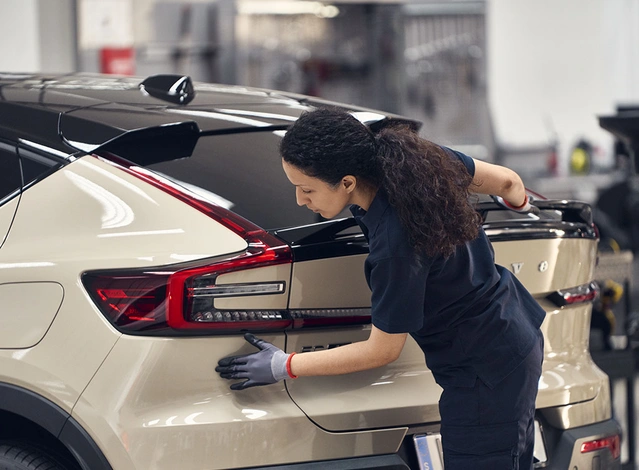 Dans un atelier Volvo, une technicienne inspecte l’arrière d’un C40 Recharge beige dans le cadre du contrôle technique.