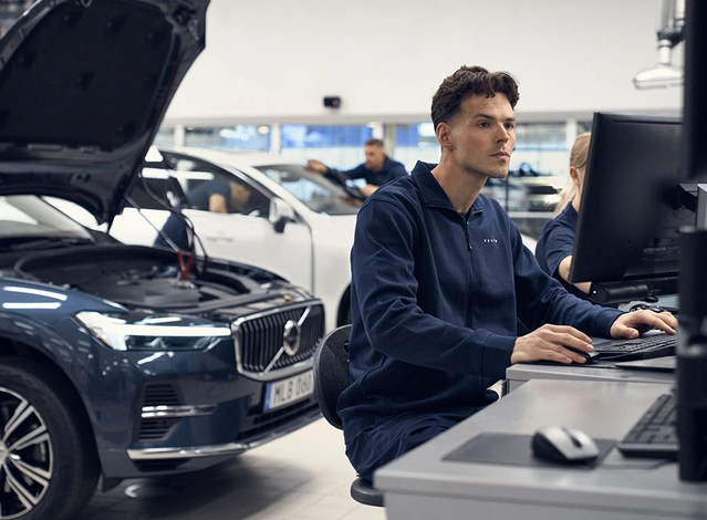 Un technicien devant son ordinateur inspecte le boitier informatique du Volvo XC60 placé derrière lui avec le capot ouvert