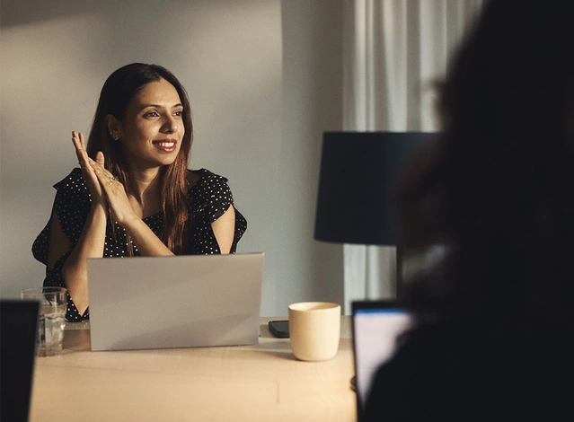Femme devant un ordinateur portable sur une table, une personne floue au premier plan.
